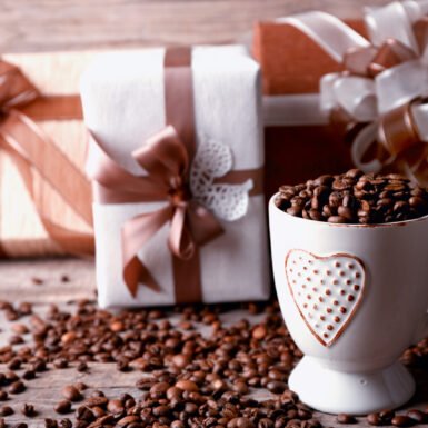 Beautiful gift with bow and coffee grains in mug, on wooden background
